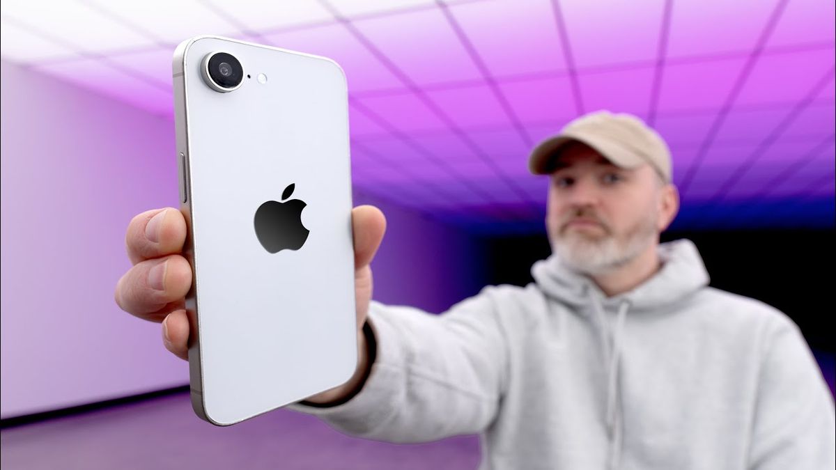 A hand holding the new iPhone 16E in front of a blurred background, showcasing its sleek design and vibrant display.